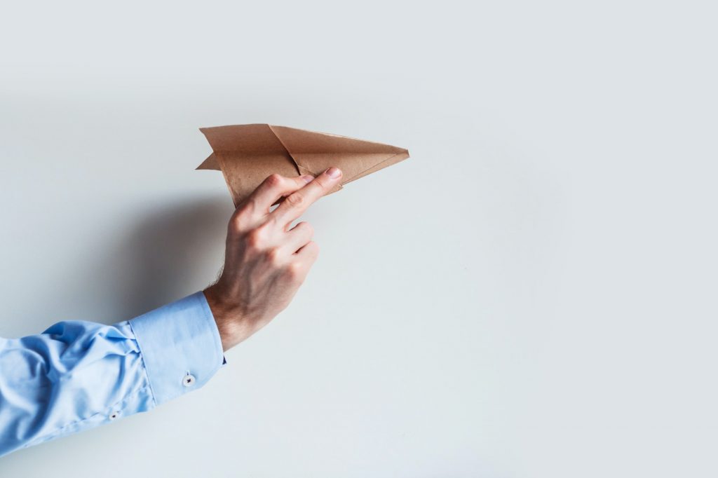 A male hand in a blue shirt uniform launches a paper airplane.